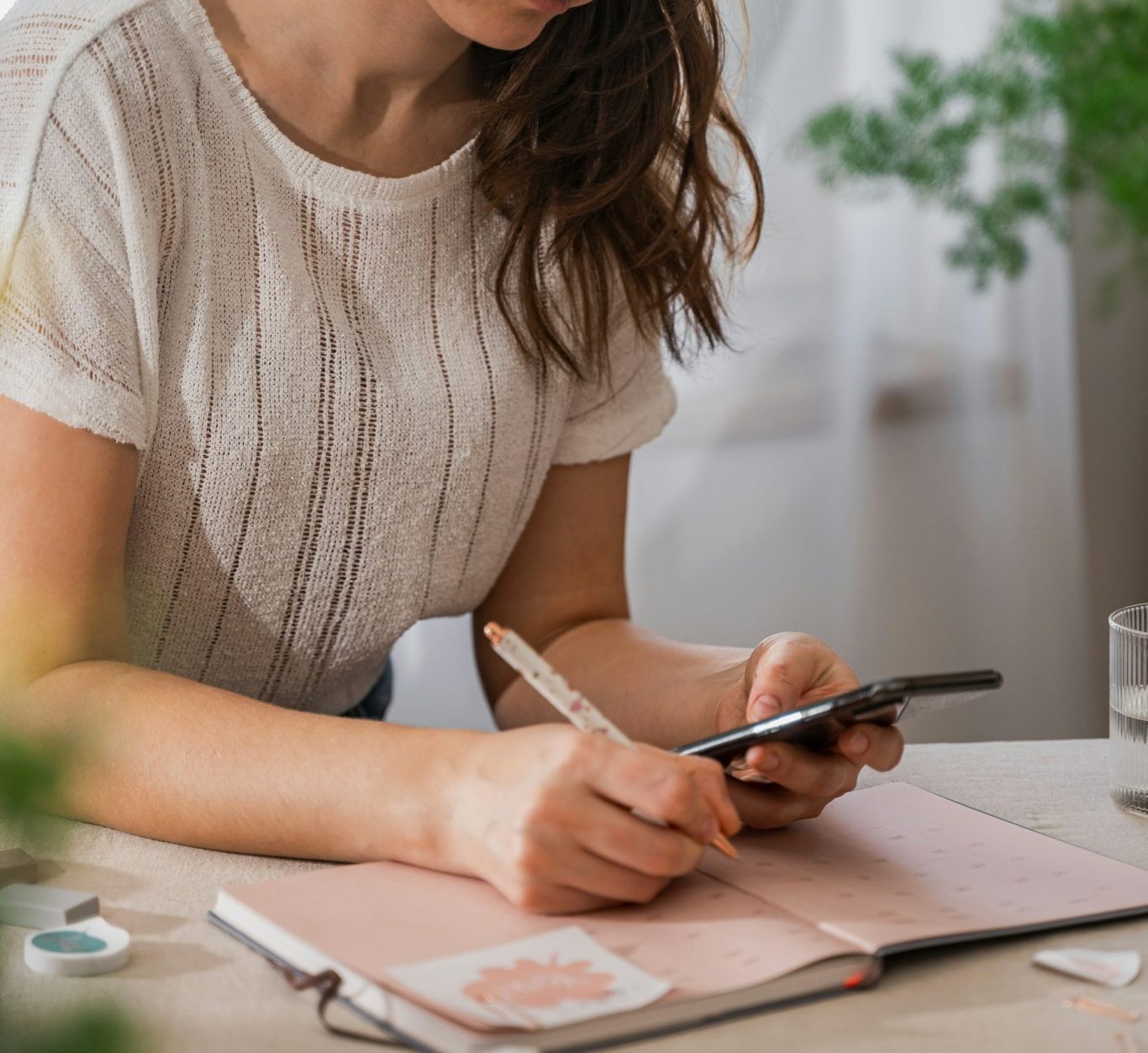 Eine Person schreibt in ein Notizbuch und hält ein Smartphone in der Hand.
