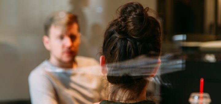 Junger Mann und Frau im Gespräch, Blick auf die Frau von hinten, Getränk auf dem Tisch.