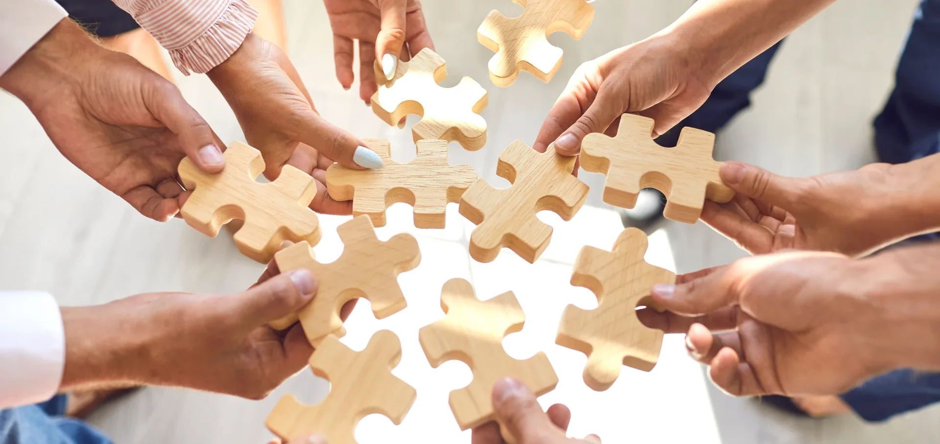 Hände greifen nach Puzzlestücken, die zusammengefügt werden sollen.