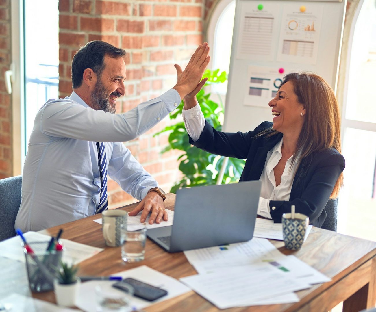 Zwei Personen in einem Büro geben sich ein High-Five, Freude und Zusammenarbeit.